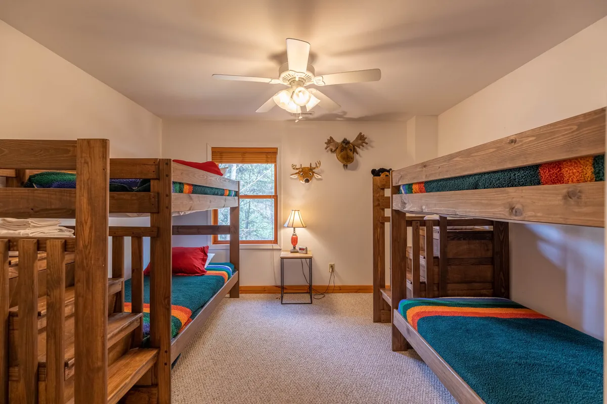 A cheerful bunk room with twin-over-twin bunk beds dressed in colorful blankets, a lamp, and a window allowing natural light to fill the space. The room exudes playfulness and comfort, making it an ideal haven for kids or single guests.