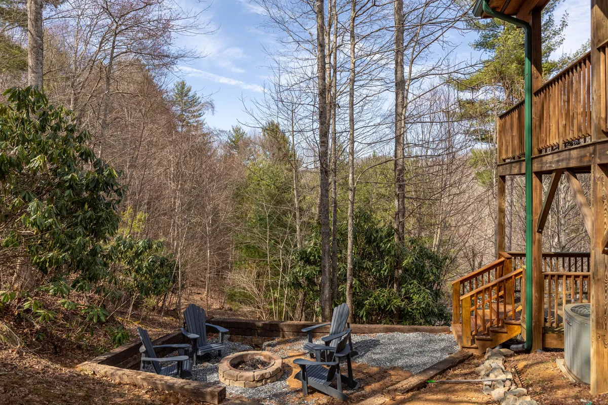A charming firepit area with Adirondack chairs arranged for conversation, set on a wooden deck surrounded by trees. The setting is perfect for starlit storytelling, roasting marshmallows, and family bonding under the night sky.