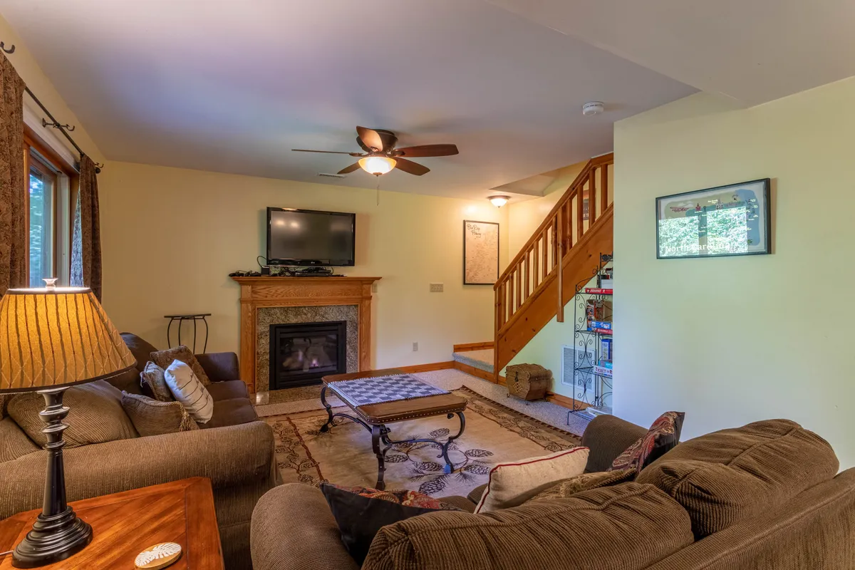 A comfortable living space featuring a warm fireplace, a plush sofa, and a coffee table, with a staircase in the background. The room is perfect for relaxing movie nights, group games, or unwinding after a day of adventure.