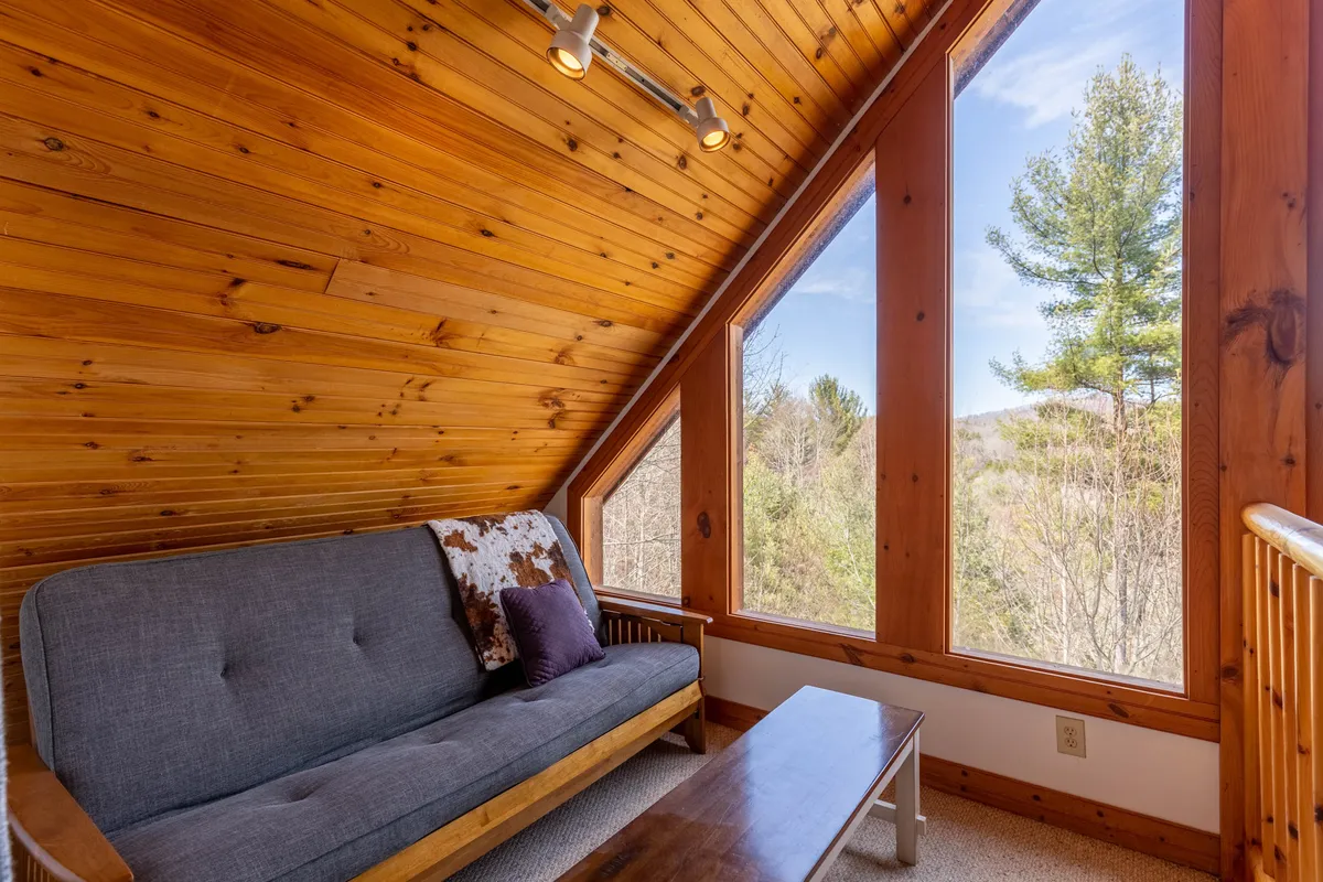 A tranquil seating area with large windows framing natural views, a comfortable sofa, a wooden coffee table, and a wooden ceiling. The space is filled with natural light and invites guests to relax while enjoying the surrounding mountain scenery.