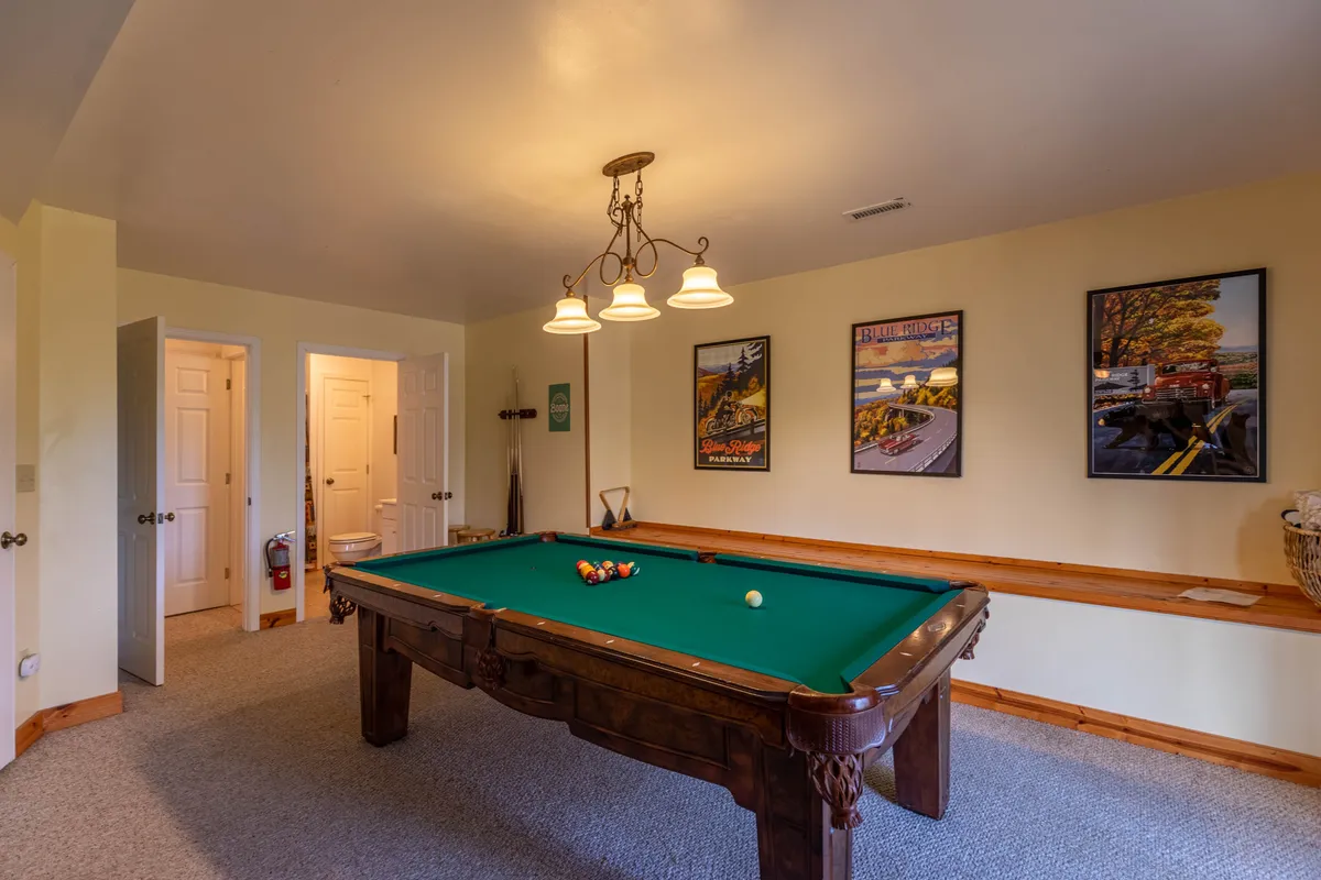 This image showcases a vibrant game room featuring a pool table at the center, stylish chandelier above, and framed posters on the walls. The scene exudes fun and leisure, inviting guests to gather for friendly competition and socializing.