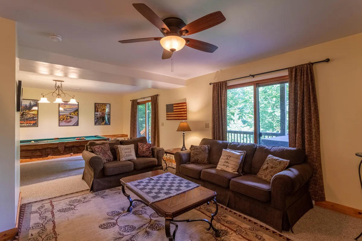 A cozy lower-level space with a pool table at the center, surrounded by a comfortable sofa seating area and a large window offering a view of the outdoors. This scene suggests a spot for both spirited games and relaxed lounging, encapsulating the family-friendly game den atmosphere.