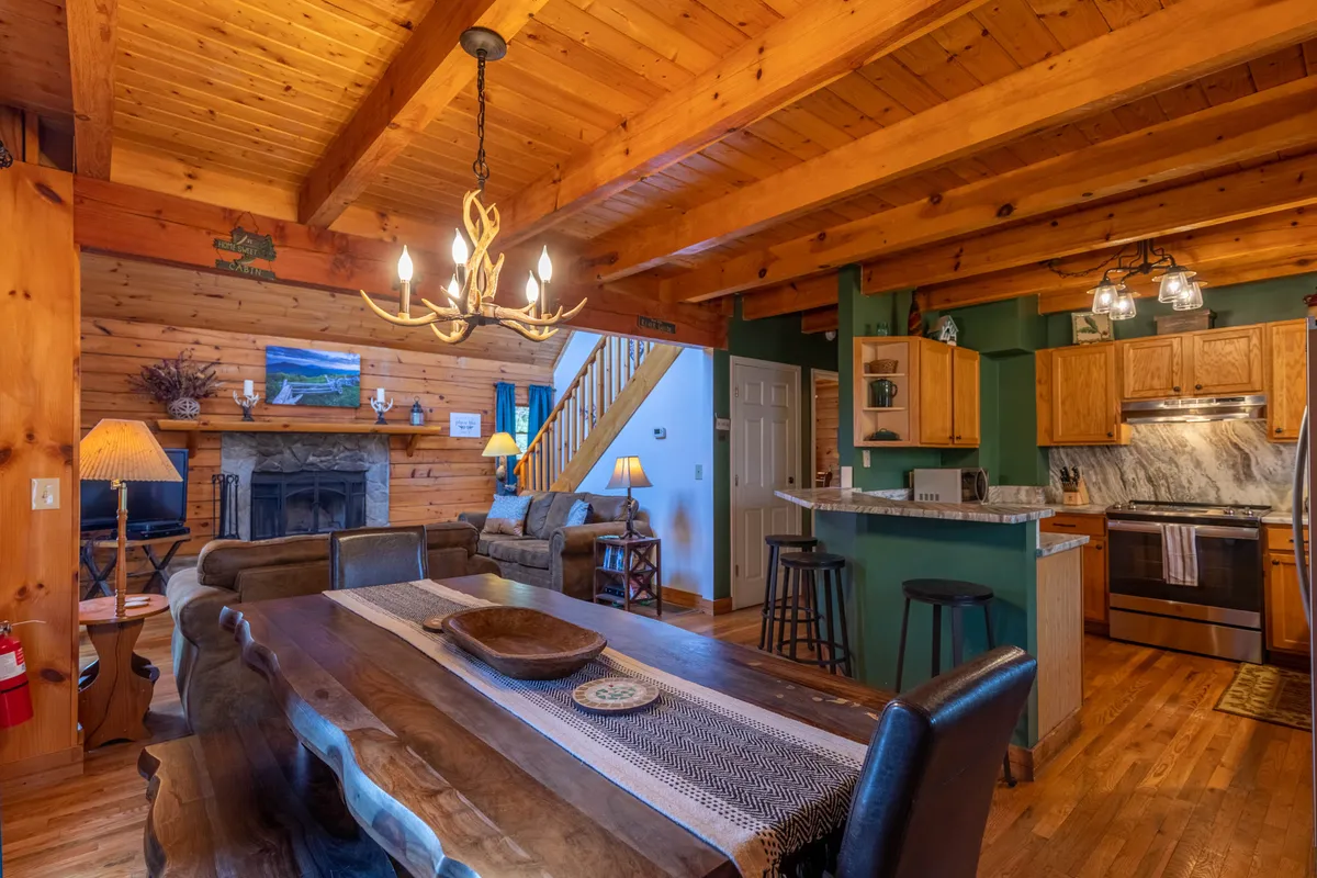 A rustic wooden dining table sits beneath a charming chandelier, with a view into the adjacent kitchen area. The ambiance is cozy and inviting, ideal for family meals, celebrations, and communal cooking.