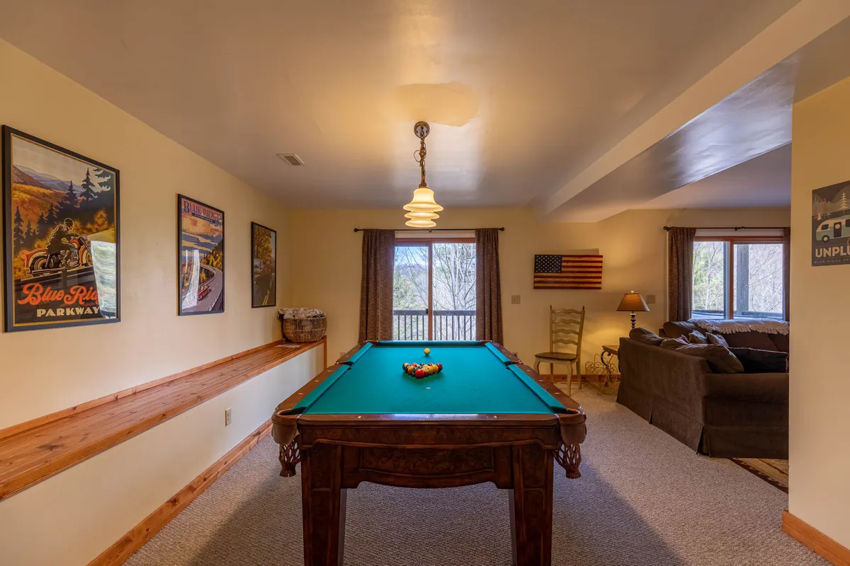 A welcoming recreation room centered around a pool table, featuring comfortable seating, game-themed posters, and a window revealing lush outdoor views. American flag accents and personal touches create a lively, homelike setting ideal for group gatherings.